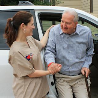 A caregiver helps an elderly man as he gets out of a vehicle, showcasing the caring bond between them.