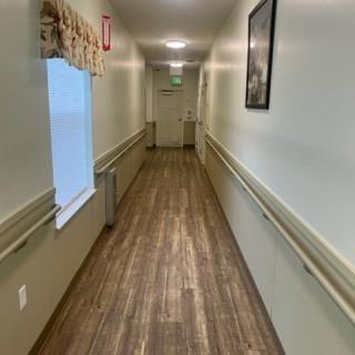 A long hallway with a wooden floor, featuring a window and wall decorations.