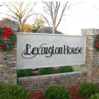 A decorative outdoor sign for Lexington House mounted on a brick wall, adorned with plants.