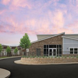 A modern school building with a brick facade and well-maintained landscaping under a colorful sky.