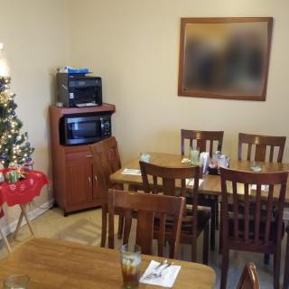 A cozy dining room with wooden furniture, a small Christmas tree in the corner, and a television on a cabinet.