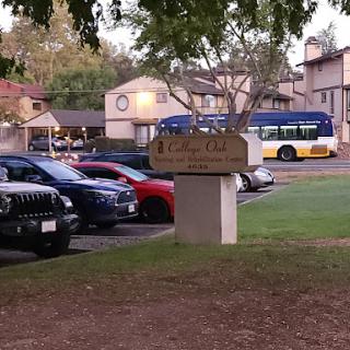 A view of a parking lot with various vehicles and an apartment complex in the background, along with a public bus.