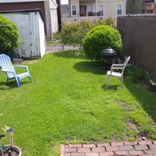 A backyard featuring a well-maintained lawn with chairs, a small grill, and a garden shed.