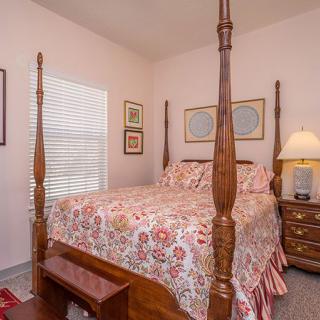 A cozy bedroom featuring a four-poster bed with decorative bedding, complemented by a nightstand with a lamp and framed artwork on the walls.