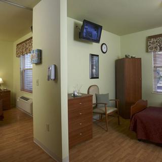A hospital room with a bed, chairs, a television, and a privacy curtain.