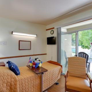 A bright and comfortable hospital room featuring two beds, a seating area, and access to an outdoor space.