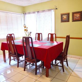 A dining room with a red tablecloth covering the table, surrounded by wooden chairs and large windows letting in natural light.