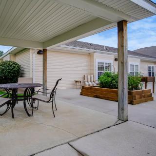 A covered patio with outdoor furniture and garden beds in a residential backyard.