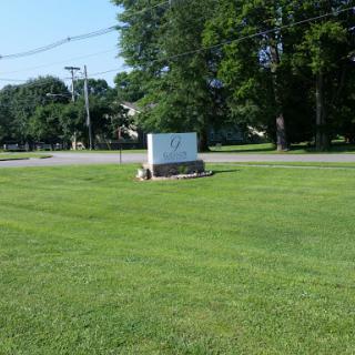 A view of a roadside sign on a sunny day, surrounded by well-maintained grass and trees.