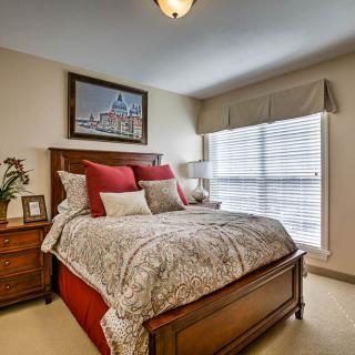 A cozy bedroom featuring a large bed with red and gray bedding, a bedside table with decor, and a picture hanging above the bed.