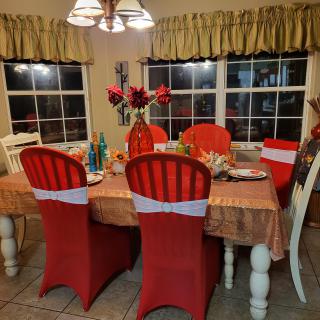 A dining room with a festive table setting, featuring red chair covers and flower arrangements.
