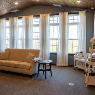 A cozy living room with a couch, multiple windows with curtains, a small table, and a crib.