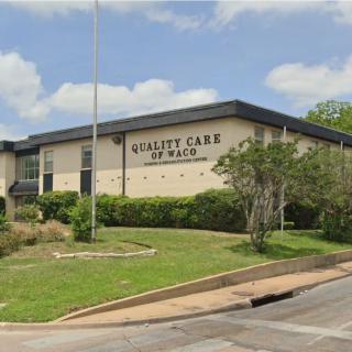 A healthcare facility named 'Quality Care' surrounded by greenery under a blue sky.