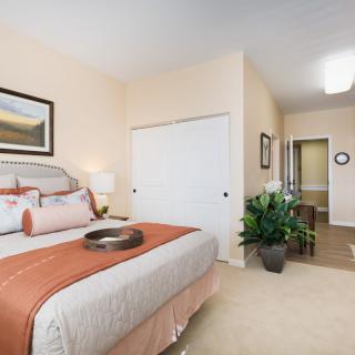 A modern bedroom with a neatly made bed, artwork on the wall, and decorative plants.