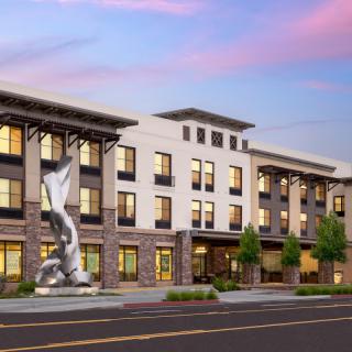 A modern building with a prominent statue in front, set against a colorful sky.
