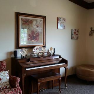 A cozy living room with a wooden piano surrounded by decorative artwork and furniture.