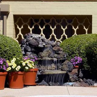 A small waterfall feature surrounded by potted flowers and shrubs in a landscaped garden.