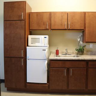A compact kitchen setup featuring wooden cabinets, a microwave, refrigerator, and sink.