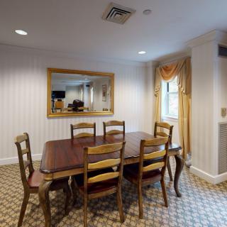 A traditional dining room with a wooden table and chairs, decorated with a large mirror and draped curtains.