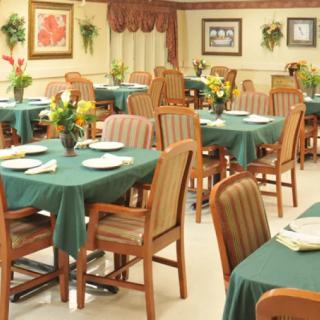 A neatly arranged dining room with tables and chairs, adorned with green tablecloths and floral centerpieces.