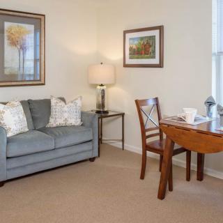 A cozy living room with a sofa, chair, and table, adorned with artwork and a lamp.