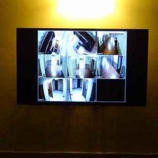 A wall-mounted monitor displaying multiple CCTV camera feeds in a hallway.