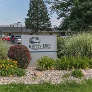 A sign for River's Edge amidst landscaped greenery with a building in the background.