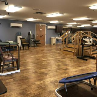 An empty gym with various exercise equipment and wooden flooring.