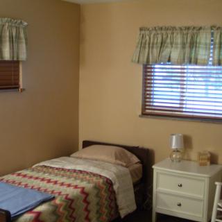 A simple bedroom with a single bed and a nightstand, featuring window blinds and floral curtains.