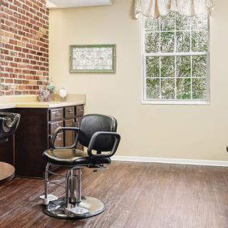 A spacious hair salon interior with a styling chair, mirror, and large window.
