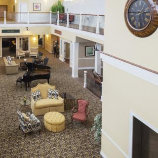 A spacious lobby with seating arrangements, a grand piano, and a large wall clock in a two-story building.