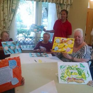Elderly individuals proudly display their paintings during an art class at a nursing home.