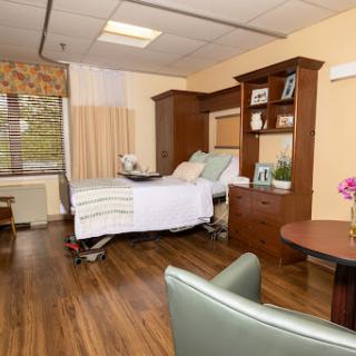 A well-lit and comfortable hospital patient room featuring a bed, seating area, and personal touches.