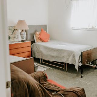A cozy bedroom with a single bed, dresser, and lamp, highlighted by natural light.