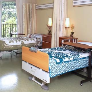 A shared hospital room with two medical beds and bedside tables, equipped with privacy curtains.