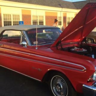 A classic red convertible with its hood open, parked in front of a building.
