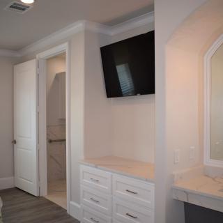 Modern bedroom with a television mounted above a dresser and an adjacent vanity mirror.