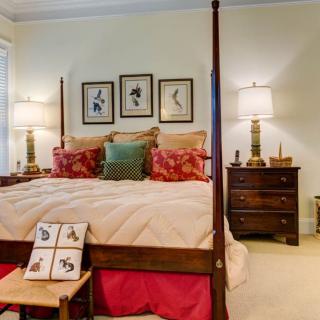 A cozy, traditionally designed bedroom featuring a four-poster bed with decorative pillows, framed artwork above the headboard, and lamps on wooden nightstands.