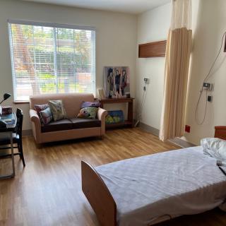 A hospital room with a single bed, a sofa, and a large window.