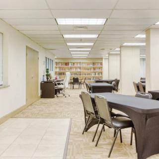 A modern office workspace featuring tables, chairs, and bookshelves.