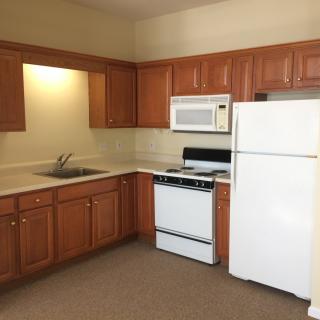 A kitchen with wooden cabinets, featuring a refrigerator, microwave, stove, and sink.