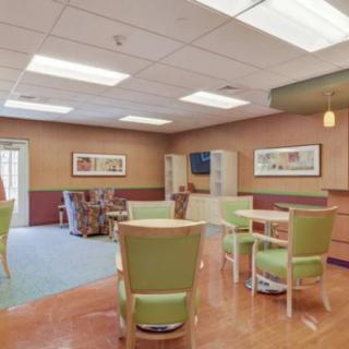 A cozy interior space featuring tables and green chairs, with artwork on the walls.