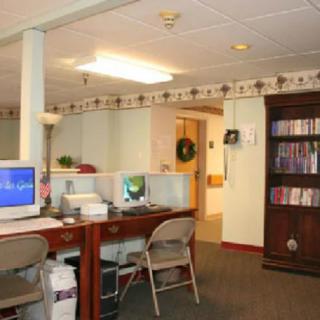 A small office space with a computer, desk, chairs, and a bookshelf.