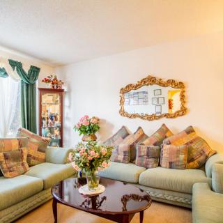 A cozy living room featuring a large sofa with patterned pillows, a decorative mirror on the wall, and a coffee table adorned with fresh flowers.