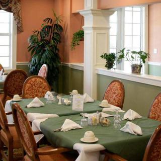 A cozy dining room with neatly set tables, adorned with plants and natural light.