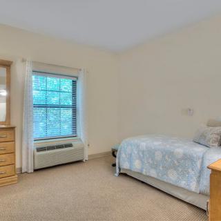 A minimalist bedroom with a single bed, dresser, and a large window.