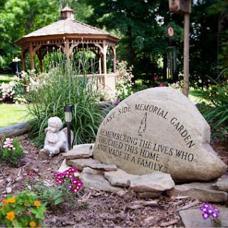 A serene memorial garden featuring a gazebo, vibrant flowers, and a stone monument honoring beloved pets.