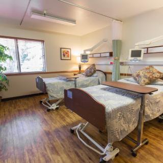 A cozy hospital patient room featuring two adjustable beds and natural light from a nearby window.