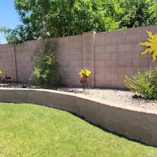 A vibrant garden area featuring a curved stone border, green grass, and colorful sun decorations against a light-colored fence.