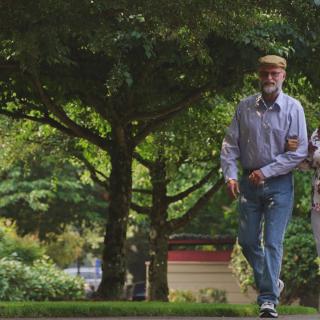 Two people walking in a park surrounded by trees.